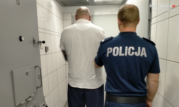 umundurowany policjant z zatrzymanym w korytarzu policyjnego aresztu, obaj stoją tyłem