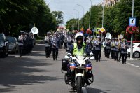 Policjant Wydziału Ruchu Drogowego na motocyklu służbowym pilotuje przemarsz kompanii, na drugim planie Orkiestra Reprezentacyjna Komendy Głównej Policji