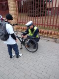 Policjant z Wydziału Ruchu Drogowego uzupełnia brakujące wyposażenie roweru uczestnikom rajdu
