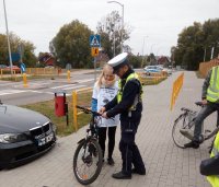 Policjant z Wydziału Ruchu Drogowego uzupełnia brakujące wyposażenie roweru uczestnikom rajdu