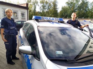 Na zdjęciu Policjanci z Ogniwa Patrolowo-Interwencyjnego Komendy Powiatowej Policji w Hajnówce stoją przy radiowozie. Po Prawej stronie radiowozu Policjant, a po lewej Policjantka.