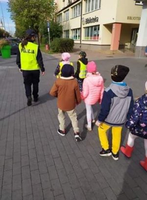 Policjantka spacerując ulicami miasta tłumaczy dzieciom zasady bezpiecznego poruszania się po drodze
