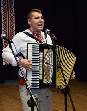 Zdjęcie przedstawia Piotrka Ostaszewskiego śpiewającego, z akordeonem.