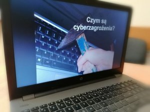Zdjęcie przedstawia laptop, na którym wyświetlana jest prezentacja o cyberzagrożeniach.