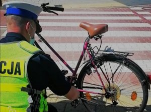 Zdjęcie przedstawiające policjanta, który sprawdza wyposażenie roweru.