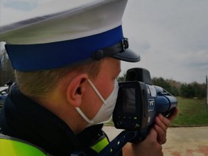 Zdjęcie przedstawia policjanta dokonującego pomiaru prędkości.