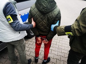 Zatrzymany obywatel Rumunii. Ma założone kajdanki z tyłu. Trzymają go policjanci kryminalni.