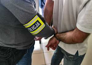 Nieumundorowany policjant zakłada obywatelowi Gruzji kajdanki.