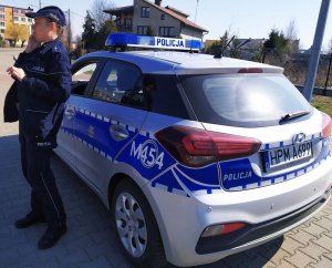 Dzielnicowa stoi przed radiowozem i rozmawia przez telefon służbowy