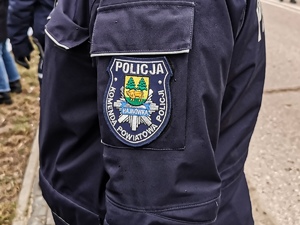 Zdjęcie przedstawia tułów umundurowanego policjanta. Na rękawie widać naszywkę z napisem Komenda Powiatowa Policji w Hajnówce.