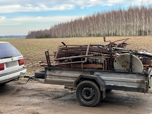 Zdjęcie przedstawia samochód osobowy koloru białego, z przyczepką samochodową. W przyczepce znajdują się luźno ułożone elementy metalowe- złom.