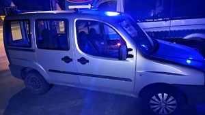 Zdjęcie przedstawia samochód marki fiat, kolor nadwozia srebrny. Na drugim planie jest widoczny radiowóz policyjny.