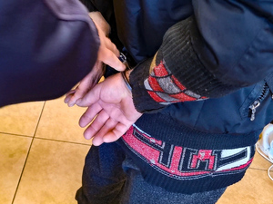 Zdjęcie przedstawia ręce zatrzymanego w trakcie zakładania kajdanek.